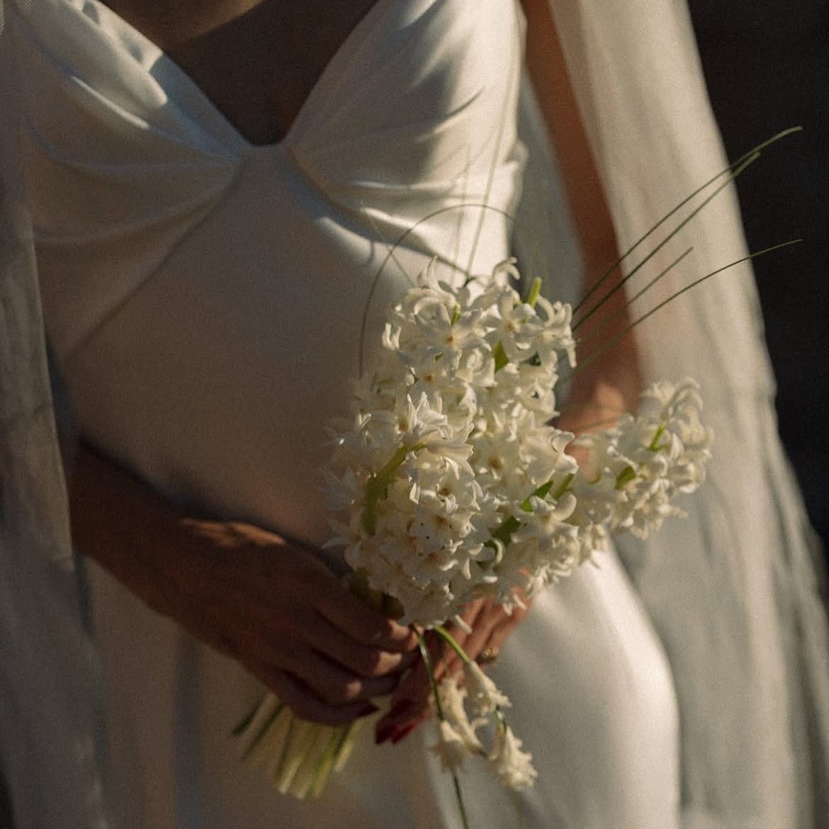 Braut mit schlichtem weißen Brautkleid. Sie hält einen kleinen Blumenstrauß mit weiß-grünen Blumen vor ihrem Bauch.
